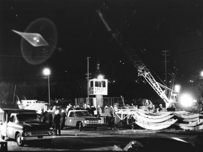 The brightly lit rescue scene at the entrance to the Sylmar water district tunnel is a harsh contrast against the dark night. Rescue workers desperately work against time, looking for possible survivors trapped inside the tunnel. Photograph dated June 25, 1971. 