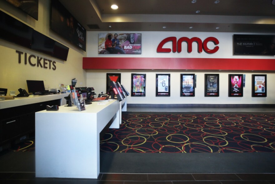 The empty ticket lobby of an AMC movie theater; the letters AMC are spelled out on the wall at the back, and movie posters hang below