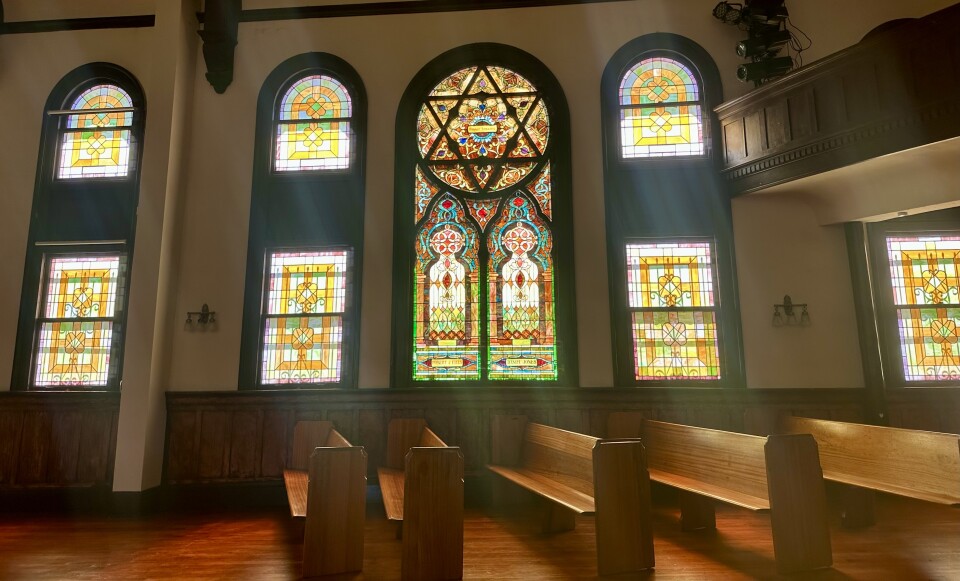 Wooden pews and stained glass with a star of David in a church. Light is shining through the windows.