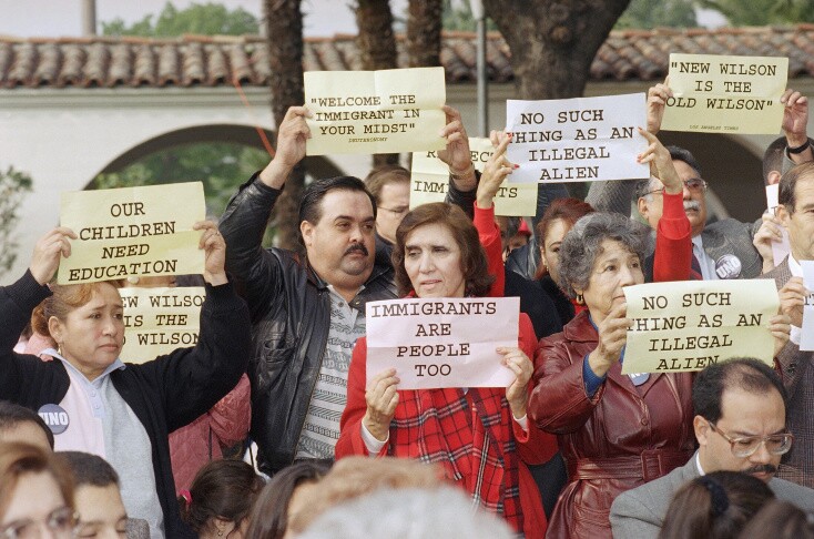 People hold signs reading: "Immigrants are people too." "Our children need an education" and others.