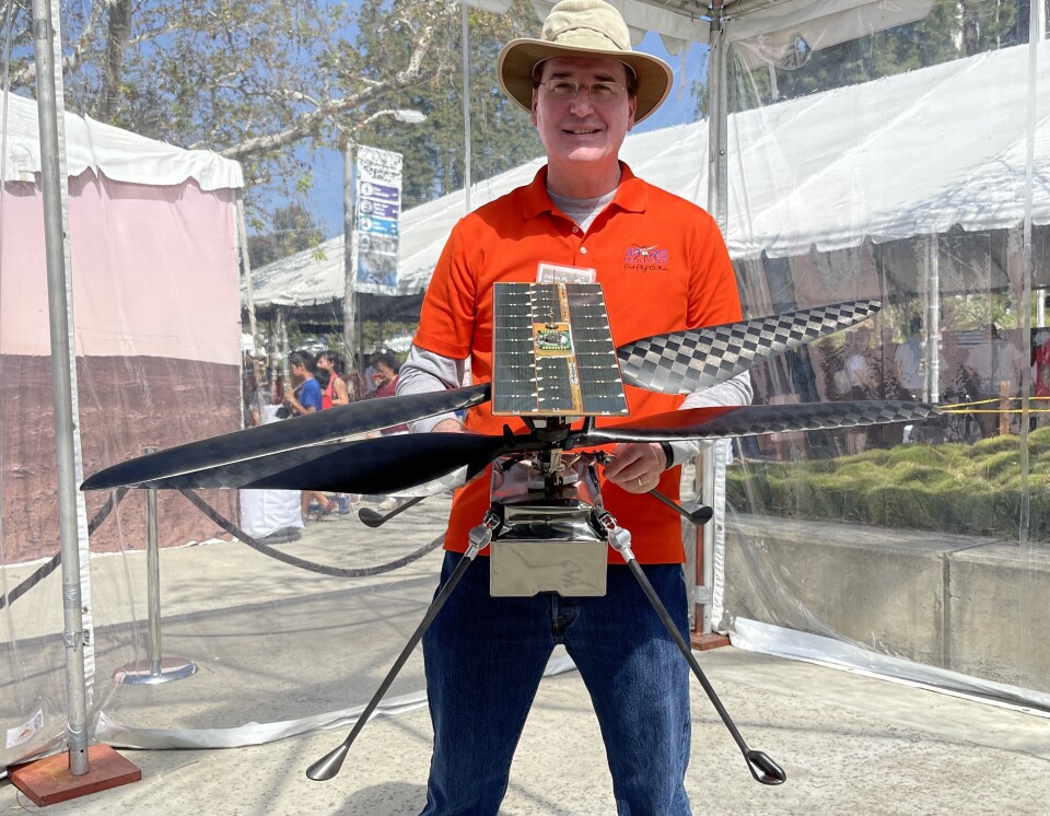 A man in an orange shirt holding a small helicopter with four blades.