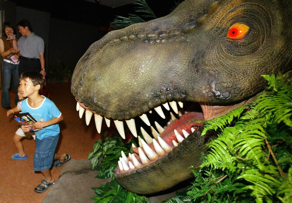 Children run away from a dinosaur at a "Jurassic Park: The Ride" display set up in a Tokyo department store on August 11, 2004 to promote Universal Studios Japan.