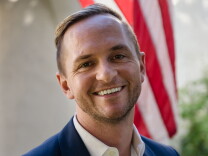 Headshot of Craig Greiwe. He's smiling and wearing a navy jacket and white collared shirt. He has a light complexion and short, blond hair cropped very close on the sides and combed to one side on the top.