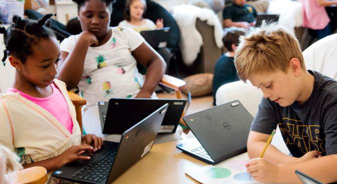 Children write and use laptops in a classroom.