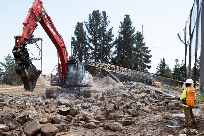 A person spraying water on a pile of rubble with a big machine moving it.