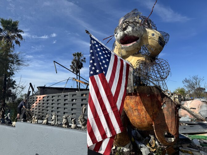 A large bunny wire topiary holding an American flag in front of a property with debris.