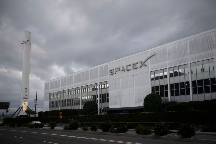 A SpaceX building next to a rocket. The sky is grey and cloudy.
