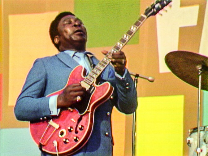 An image of blues musician B.B. King in a blue suit playing a red guitar, as seen in the documentary "Summer of Soul"