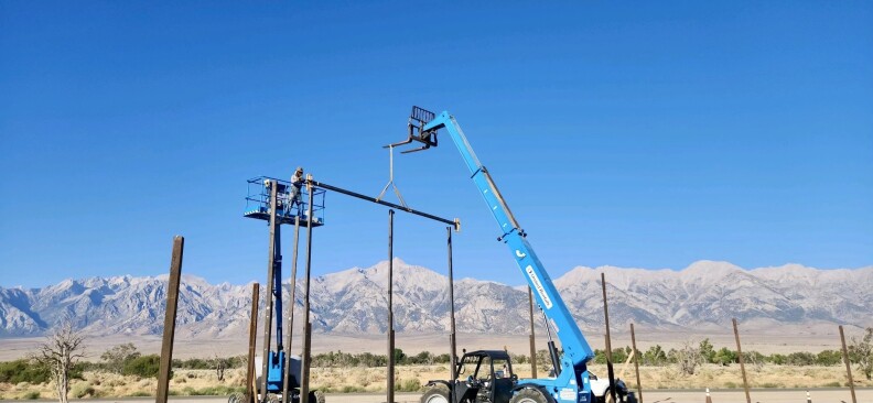 A crane lowers a beam and tall mountains are in the background