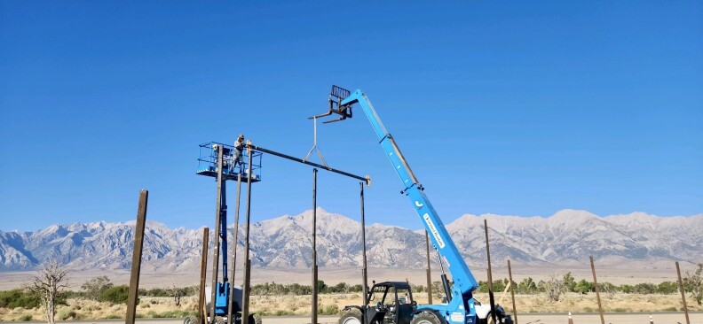 A crane lowers a beam and high mountains can be seen in the background