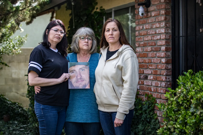 Three women stand side by side, one holding a memorial photo of a young man.