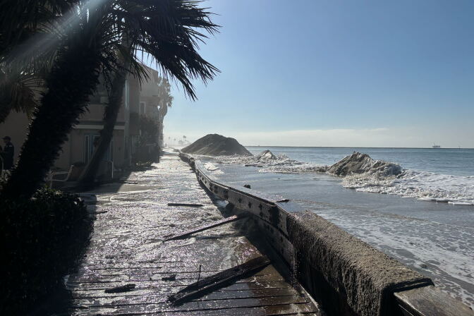 A flooded boardwalk along a coastline with eroded sand berms.