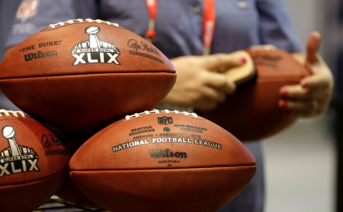 An employee of the Wilson Sporting Goods Co. puts the finishing touches on a replica Super Bowl XLIX football at the NFL Experience Saturday, Jan. 24, 2015, in Phoenix. The company set up a production line to manufacture the footballs which are sold to the public at the event. (AP Photo/Charlie Riedel)