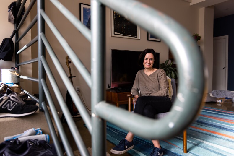 Karin Tracy in the living room of her Downtown L.A. apartment. She is framed through metal railing running alongside a couple of steps.