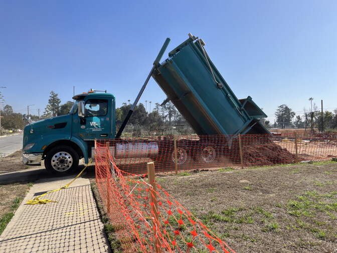 A large truck dumps mulch on an open property. 