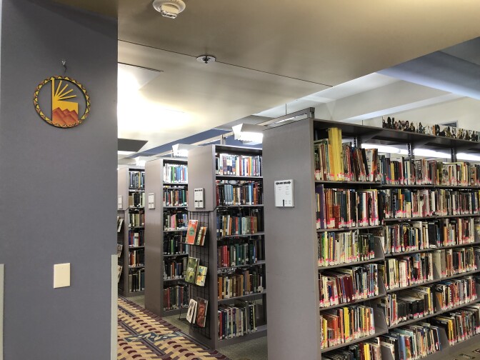 Three rows of grey bookshelves filled with different books in different colors at the Los Angeles Public Library. On the side of each shelf is a small white rectangle that serves as a sign saying what section the shelf is.