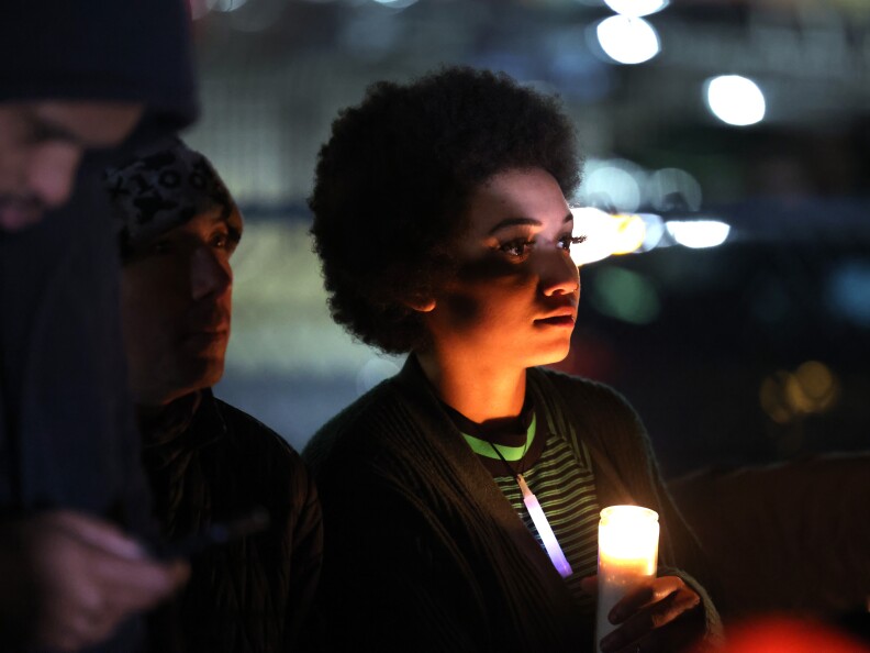 A person with dark-tone skin and curly hair holds a single candle