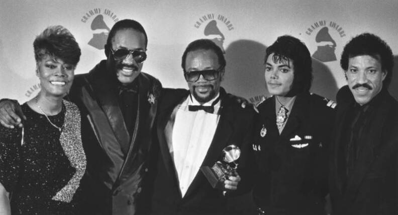A group of five people smile for a photo, one with a Grammy Award in his hand.
