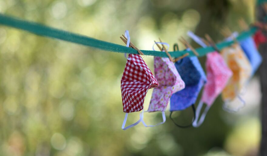 Masks in various colors are hung on the clothesline with a green background from trees.