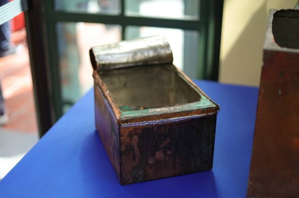 A close up of a smaller empty metal box that's been pried open on a blue table. The lid rolls back into itself.