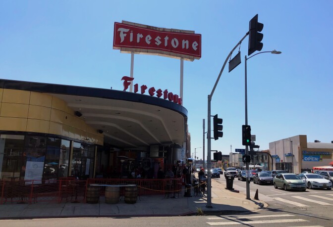 the exterior of a beige Streamline Moderne building with a big red Firestone sign above the building.