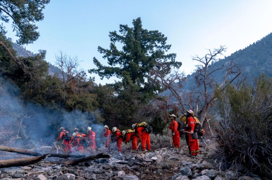 A crew of inmate firefighters walking through smoldering matter.