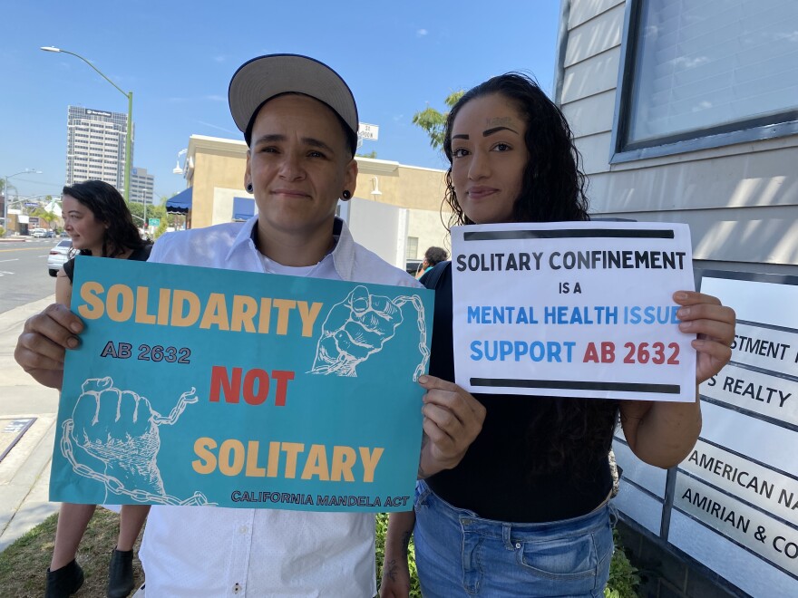 Rojas and Maria Alvarado hold signs at a rally calling for restrictions on solitary confinement. Rojas wears a white shirt and holds a blue sign that reads "Solidarity not solitary." Alvarado holds a sign that reads "Solitary Confinement is a Mental Health Issue. Support AB 2632"