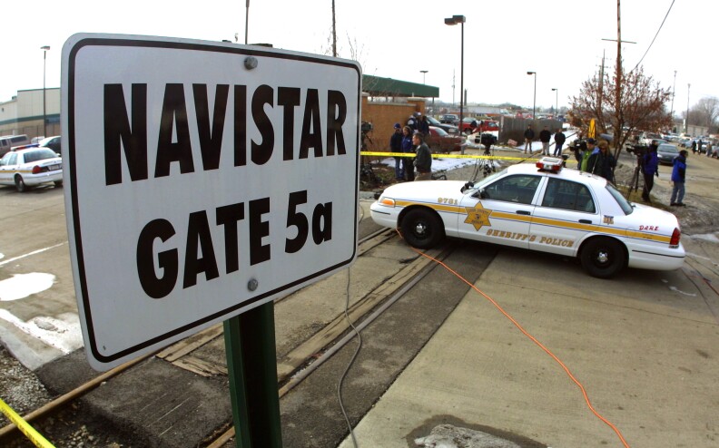A sign reads "Navistar Gate 5a" stands near a sheriff's car with police tape around the area.