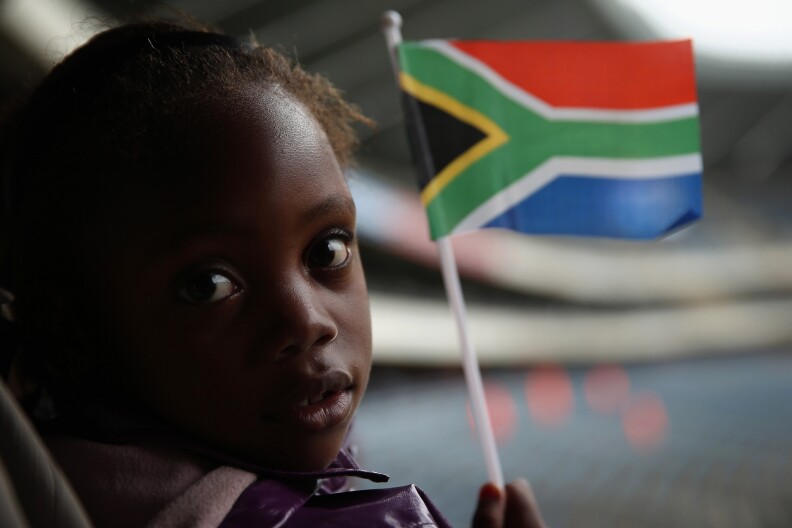 JOHANNESBURG, SOUTH AFRICA - DECEMBER 10:  A girl waves a South African flag while watching the official memorial service for Nelson Mandela on a large screen inside the Orlando Stadium in Soweto, on December 10, 2013 in Johannesburg, South Africa. Over 60 heads of state have travelled to South Africa to attend a week of events commemorating the life of former South African President Nelson Mandela. Mr Mandela passed away on the evening of December 5, 2013 at his home in Houghton at the age of 95. Mandela became South Africa's first black president in 1994 after spending 27 years in jail for his activism against apartheid in a racially-divided South Africa.  (Photo by Dan Kitwood/Getty Images)