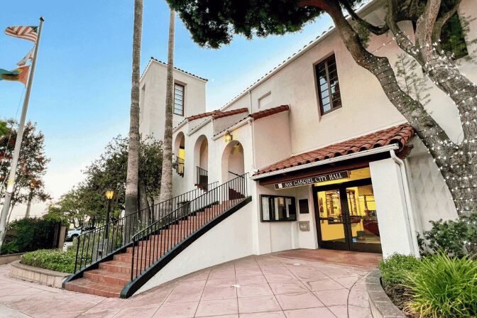 A Spanish-style building has a tiled exterior staircase and a sign above a first floor entrance that reads: San Gabriel City Hall