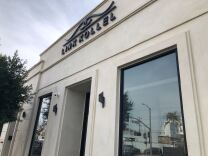 The exterior of a building has smooth stucco and large windows reflection other buildings. The building has a sign reading: LINK KOLLEL