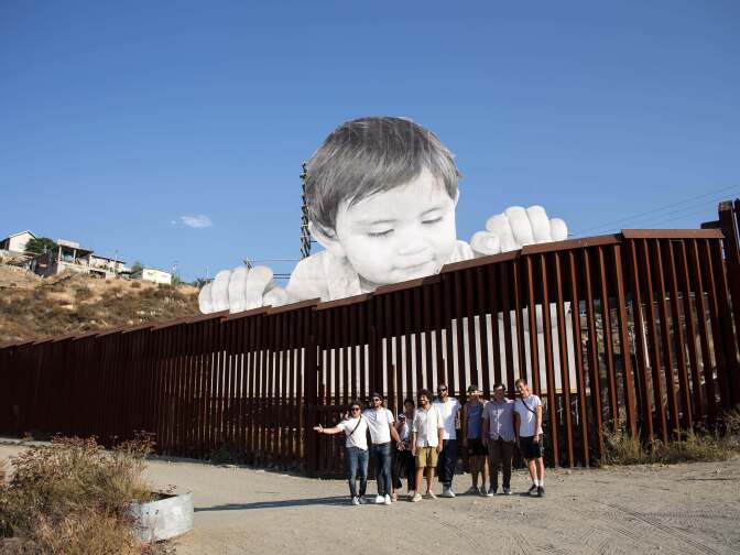 French artist JR (2-L) poses for a group photo near his artwork on the US-Mexico border in Tecate, California, United States on September 6, 2017.