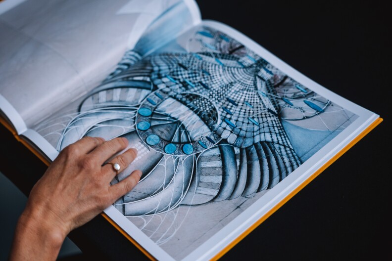 A hand on an open book with a blue art piece on the page.