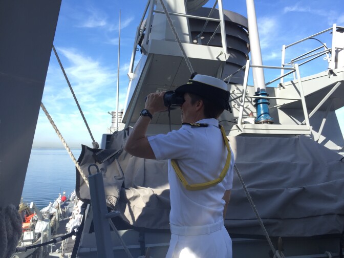 Commander Mary Katey Hays scans the channel astern of USS Decatur to ensure the ship won't collide with any other vessels as the ship backs out of her berth.