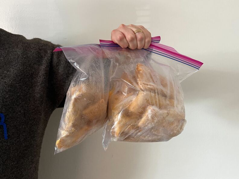 An arm holds two clear zip lock bags of the tamales