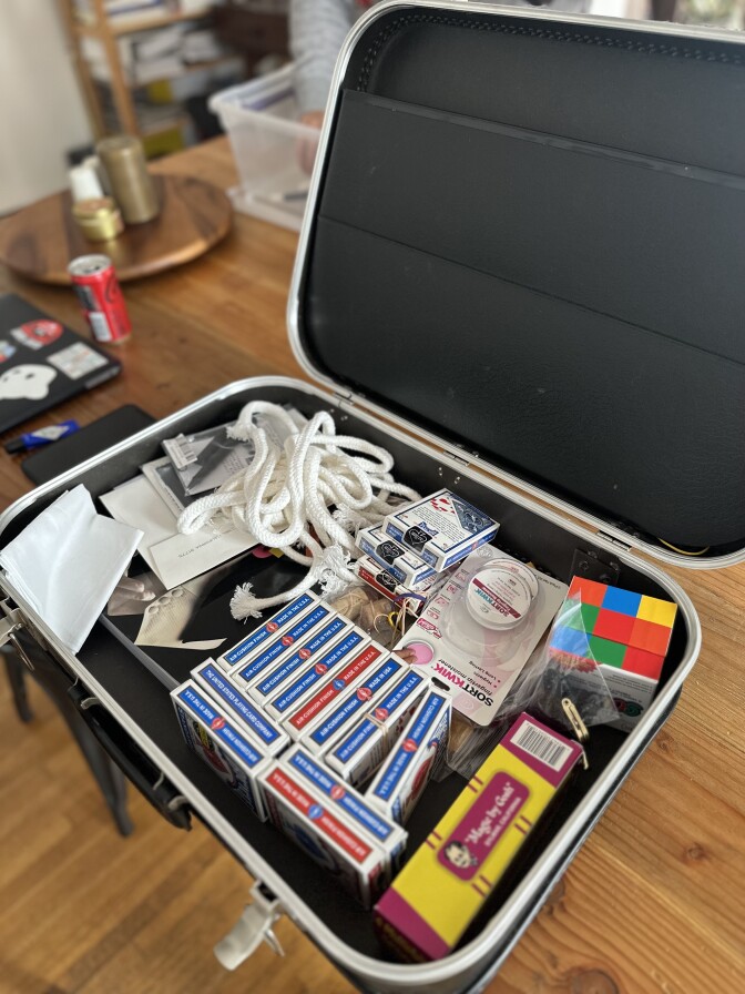 An open black suitcase is filled with magicians' supplies, including a rope, a Rubik's cube and playing cards