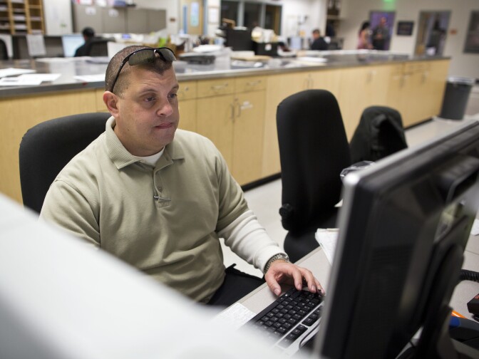 SMART Unit Police Officer Garett Bush looks into the arrest records for a man in custody with possible mental health struggles at the LAPD's Rampart Division on Thursday, Dec. 11, 2014.