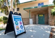 A wide image of a sign reading "Cooling center now open" in front of a tan building.