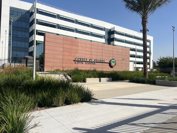 The exterior of a building has a reddish wall bearing the words "County of Orange Civic Center" and the seal of Orange County.