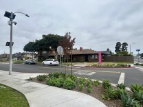A street corner with a light pole on the sidewalk affixed with a license plate reader and 360-degree camera.