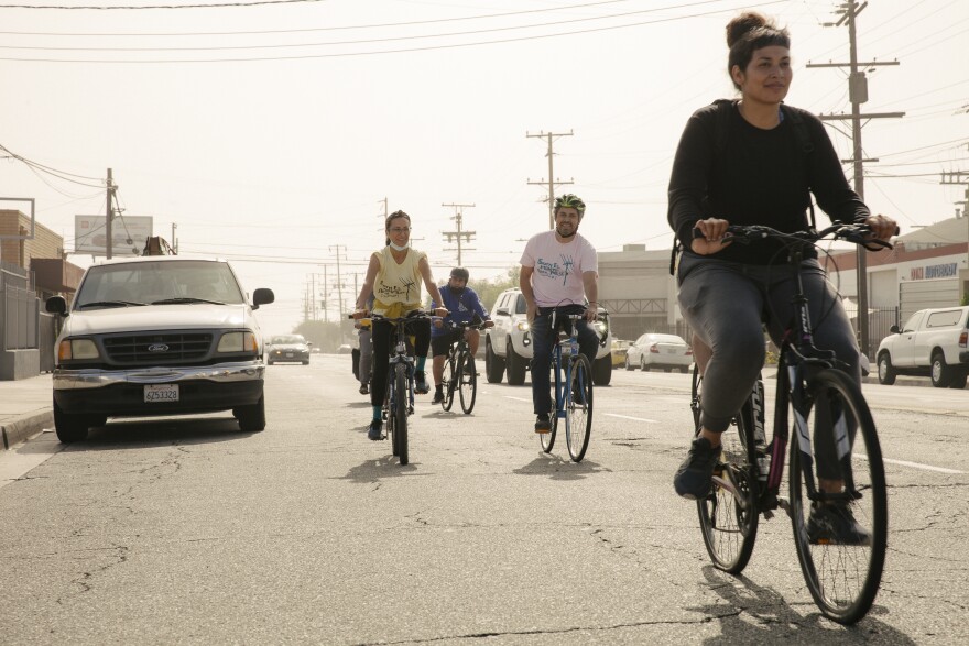 On a sunny, hazy day, a group of cyclists rides down a street.