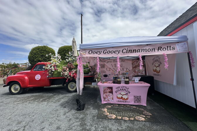 Photo of a truck next to a pop-up business. The pop-up business had a banner titled "Ooey Gooey Cinnamon Rolls." Another banner, on top of a table, has a label saying "The Little Sugarplum."