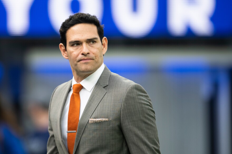 A man with dark hair is seen in a gray suit and orange tie.