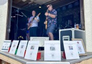 A band plays on stage behind a semi-circle of notices with QR codes to donate to victims of the Cook's Corner mass shooting. 