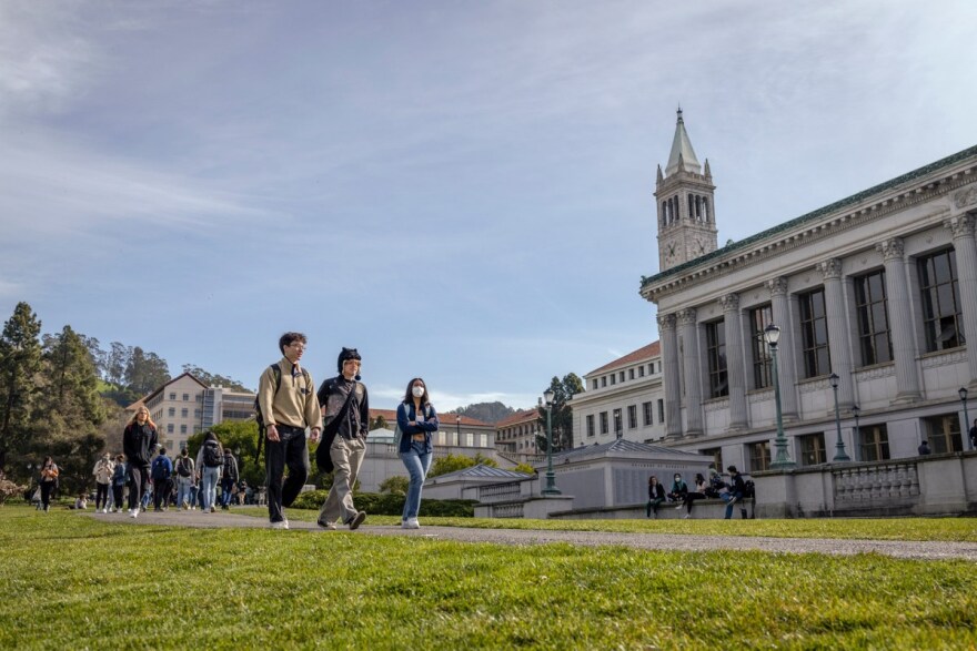 A group of students walk outside near green grass. There is a large campus building by them.