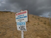 A sign on a brown grass hill reads "no trespassing property of socal gas" under stormy skies. 