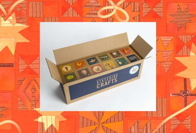 Picture of a cardboard box with blue labeling on the side that say Stateside Crafts. The top of the box is open, revealing 12 different squares of different colors, fonts and images, but all are beer centric. These are the 12 beers of Christmas, as selected by the store. The photo is positioned against a festive orange-and-gold background featuring stars, wrapped gift boxes and strands of ribbon.