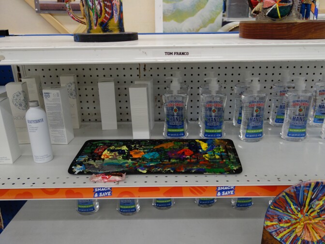 Hand sanitizer bottles on the same store shelf shelf as works of outsider art.
