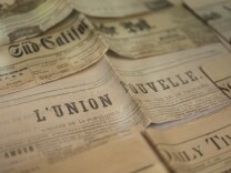 A series of yellowing newspapers with different headlines. The one in the middle says L'union nouvelle