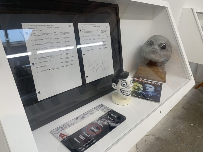 Behind a pane of glass sit some "X-Files"-related artifacts in front of what appear to be sheets of notes.